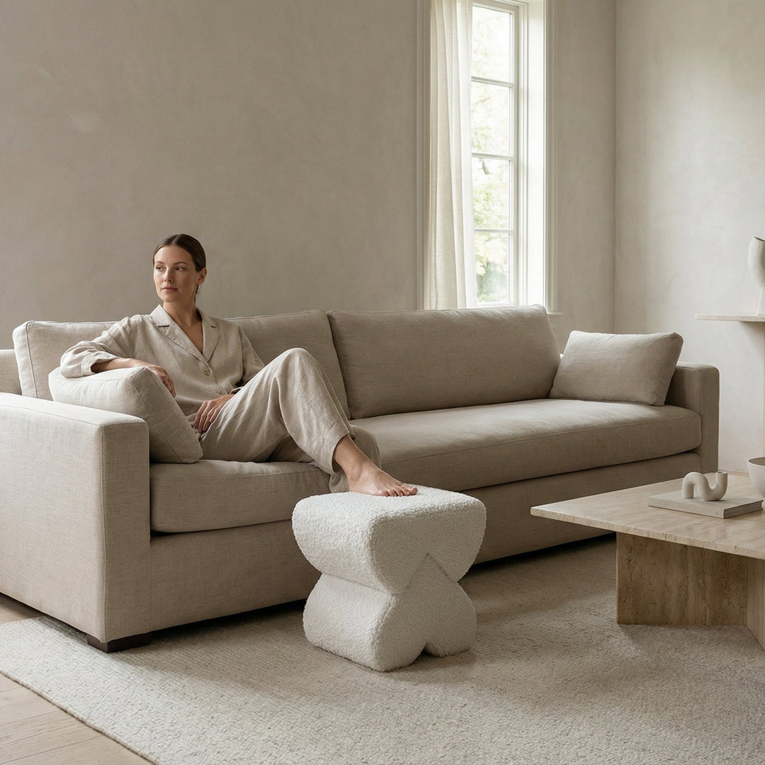 Woman sitting on a beige sofa in a minimalistic living room with a wooden coffee table and white rug.